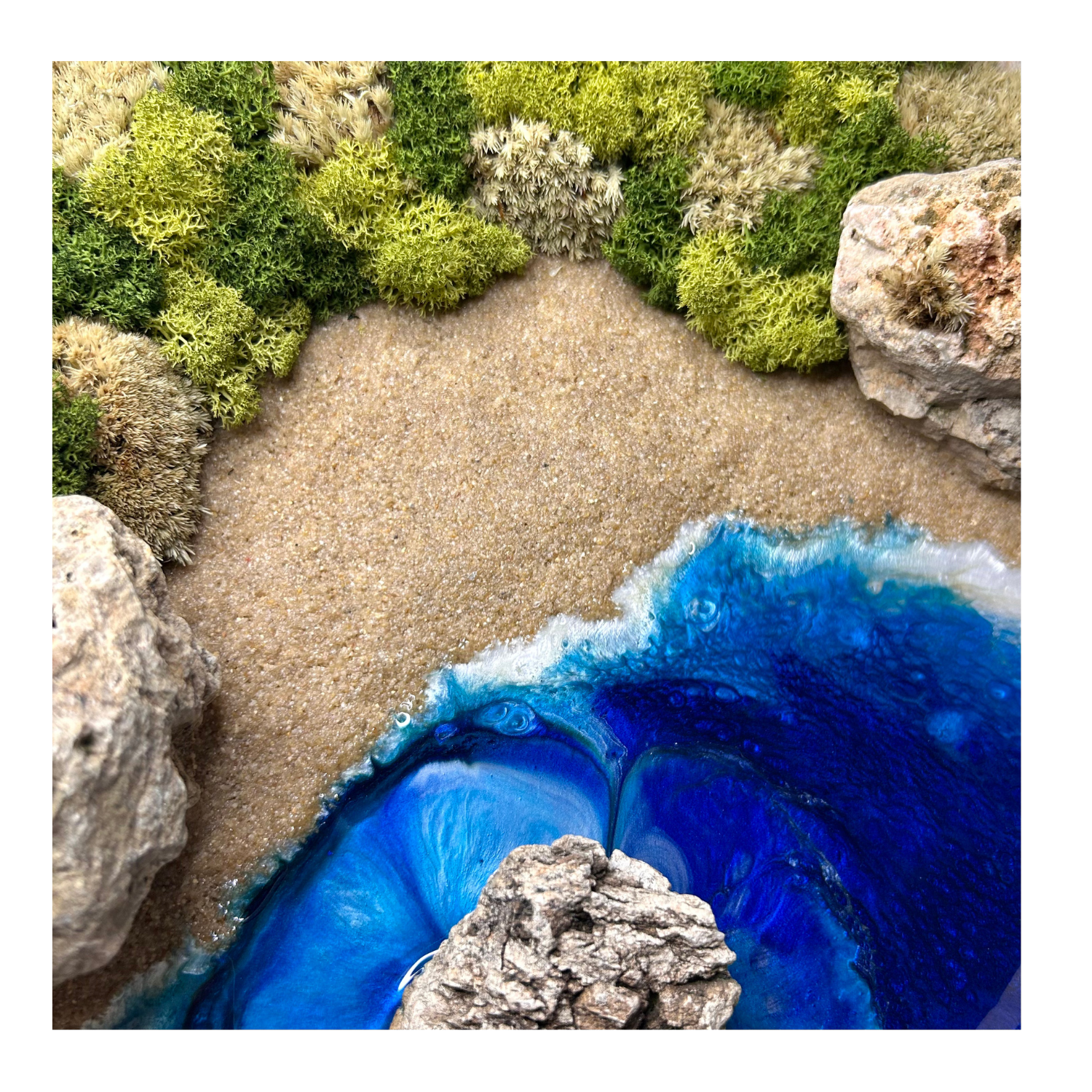 Detailansicht: Moos- und Meerbild "Goldstrand" im natürlichen runden Holzrahmen mit Sandstrand, hellen Steinen und einem Meer aus blauem Epoxidharz. Mit viel Liebe zum Detail feinste Moosspitzen aus konserviertem Moos eingebaut.