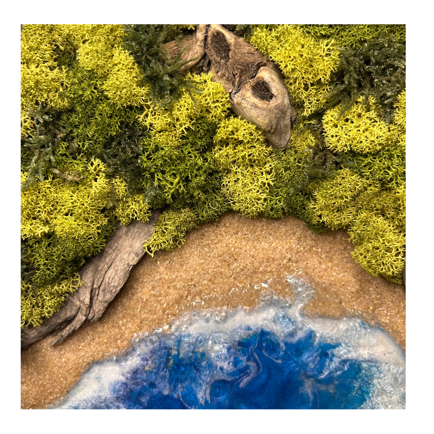 Moos- und Meerbild "Küstenpfad" im schwarzen runden Holzrahmen mit Sandstrand und einem Meer aus blauem Epoxidharz. In das Bild ist Treibholz eingebaut und mit viel Liebe zum Detail feinste Moosspitzen aus konserviertem Moos eingebaut, die teilweise aussehen wie Palmwedel.