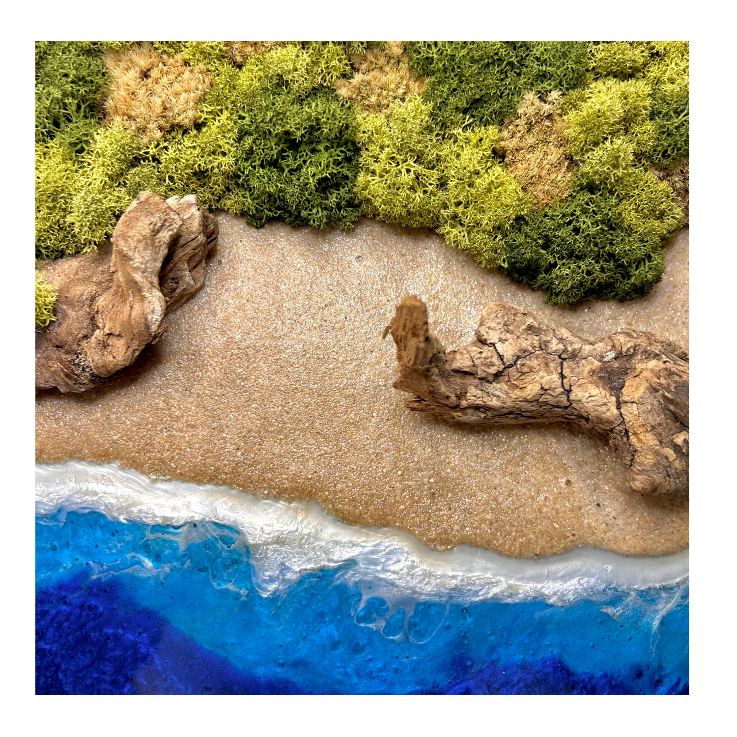 Detailansicht des Moosbildes "Treibholzstrand" im natürlichen, runden Holzrahmen mit Strand und einem Meer aus blauem Epoxidharz. Statt Steinen habe ich Treibholz eingebaut und mit viel Liebe zum Detail feinste Moosspitzen aus konserviertem Moos eingebaut.