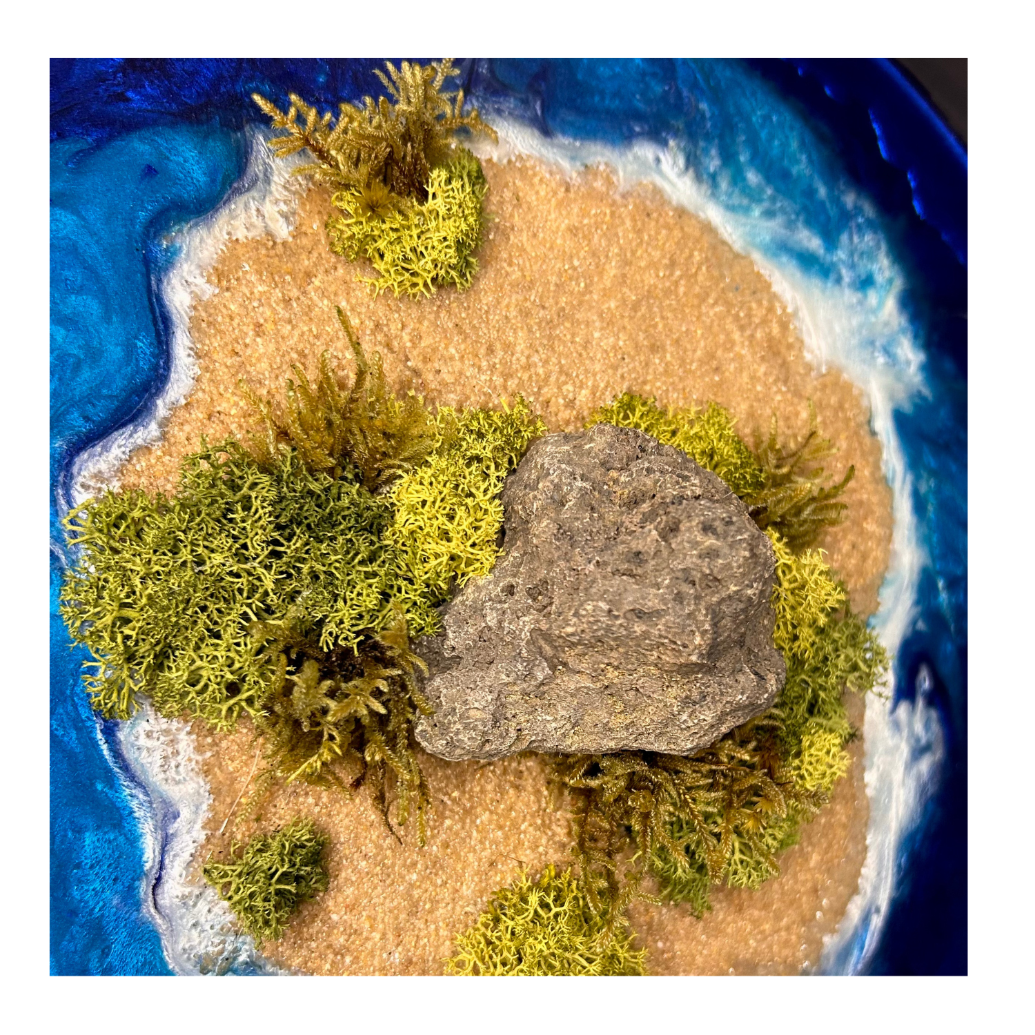 Detailaufnahme der Insel. Moos- und Meerbild mit einer einsamen Insel in der Mitte mit Moos, Sand und echtem Stein, umgeben von einem blauen Meer aus Epoxidharz. 