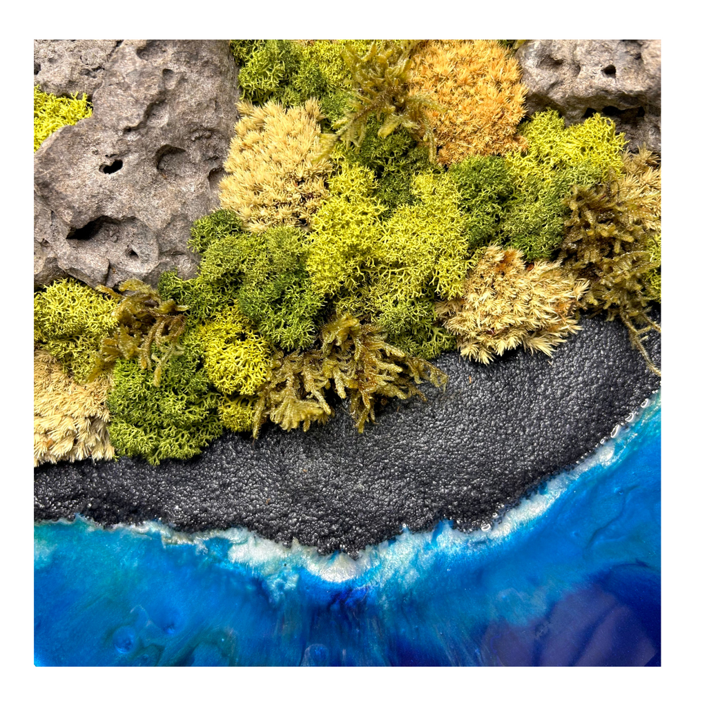 Detailansicht: Moos- und Meerbild "Küste Hawaiis" im schwarzen runden Holzrahmen mit schwarzem Strand und einem Meer aus blauem Epoxidharz. In das Bild sind natürliche Lavasteine eingebaut und mit viel Liebe zum Detail feinste Moosspitzen aus konserviertem Moos eingebaut, die teilweise aussehen wie Palmwedel. 