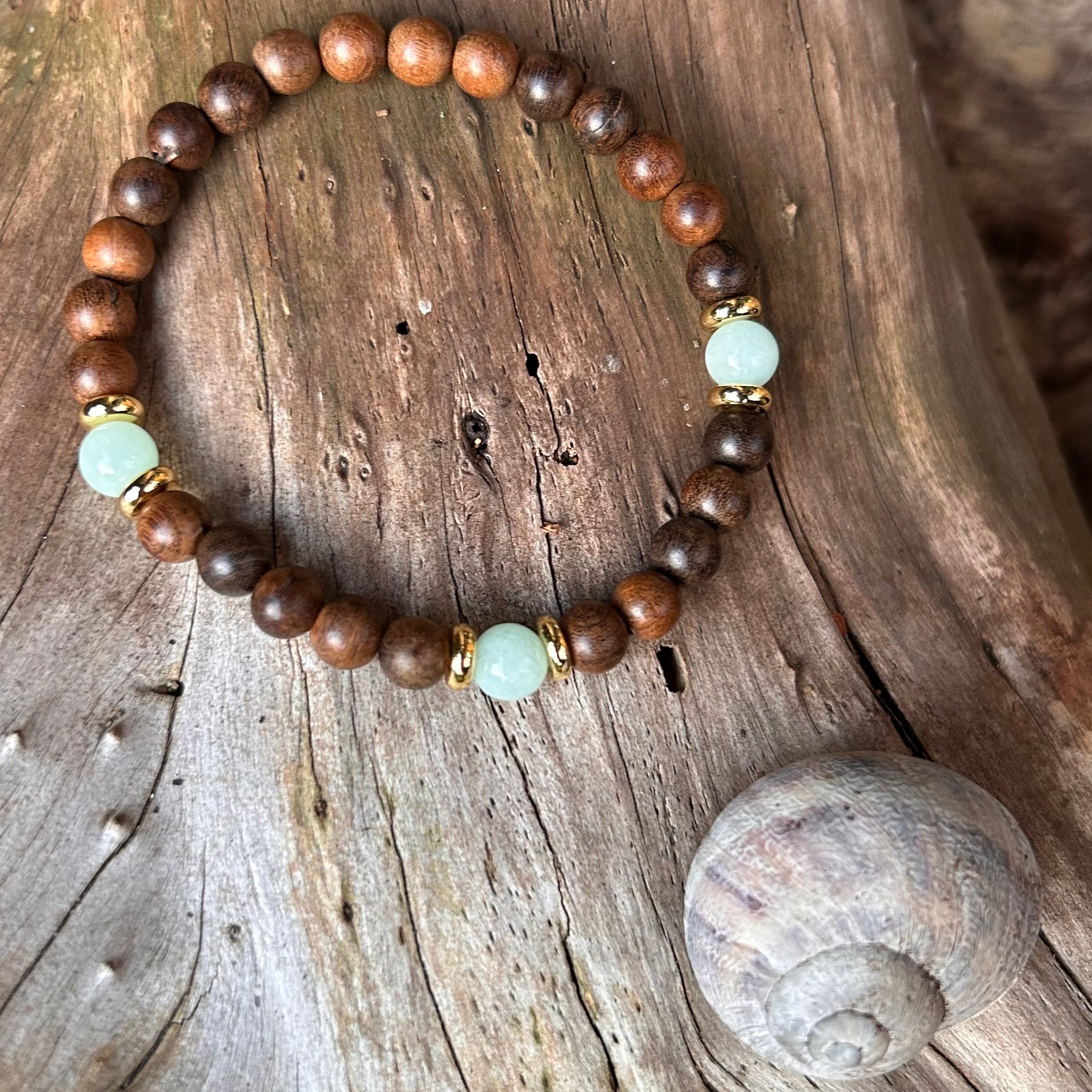 Schlichtes Armband aus naturbelassenem Sandelholz mit drei Amazonit-Perlen und vergoldeten Elementen, fotografiert auf hellem Holz mit Schneckenmuschel