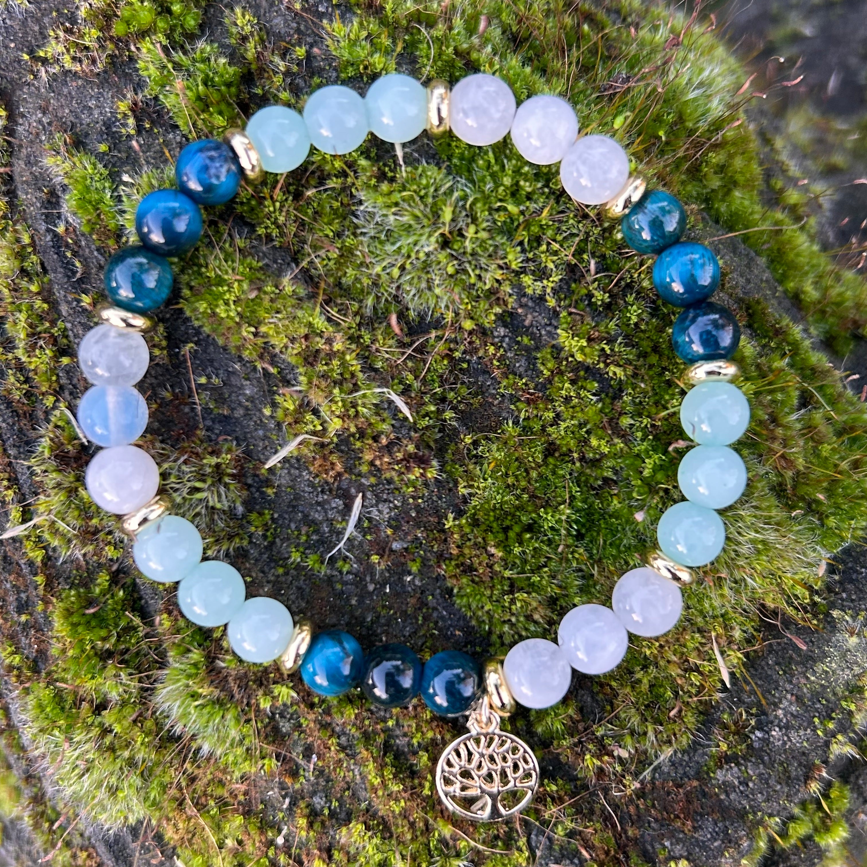 Armband aus Mondstein, Amazonit und blauem Tigerauge mit vergoldetem Lebensbaum-Anhänger auf moosbewachsenem Stein