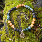 Armband mit versteinertem Holz, Moosachat, Lava und vergoldetem Lebensbaum-Anhänger auf moosbedecktem Stein