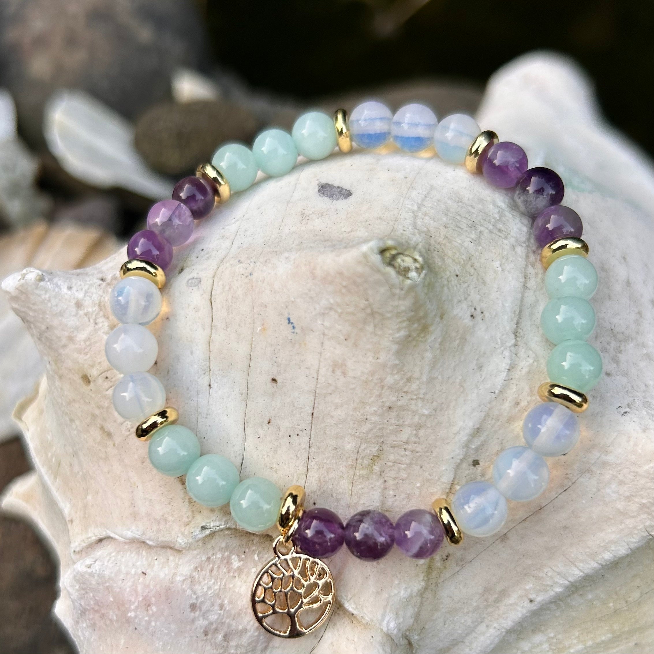 Handgefertigtes Armband aus Amazonit, Mondstein, Amethyst mit vergoldetem Lebensbaum-Anhänger, auf einer Muschel arrangiert