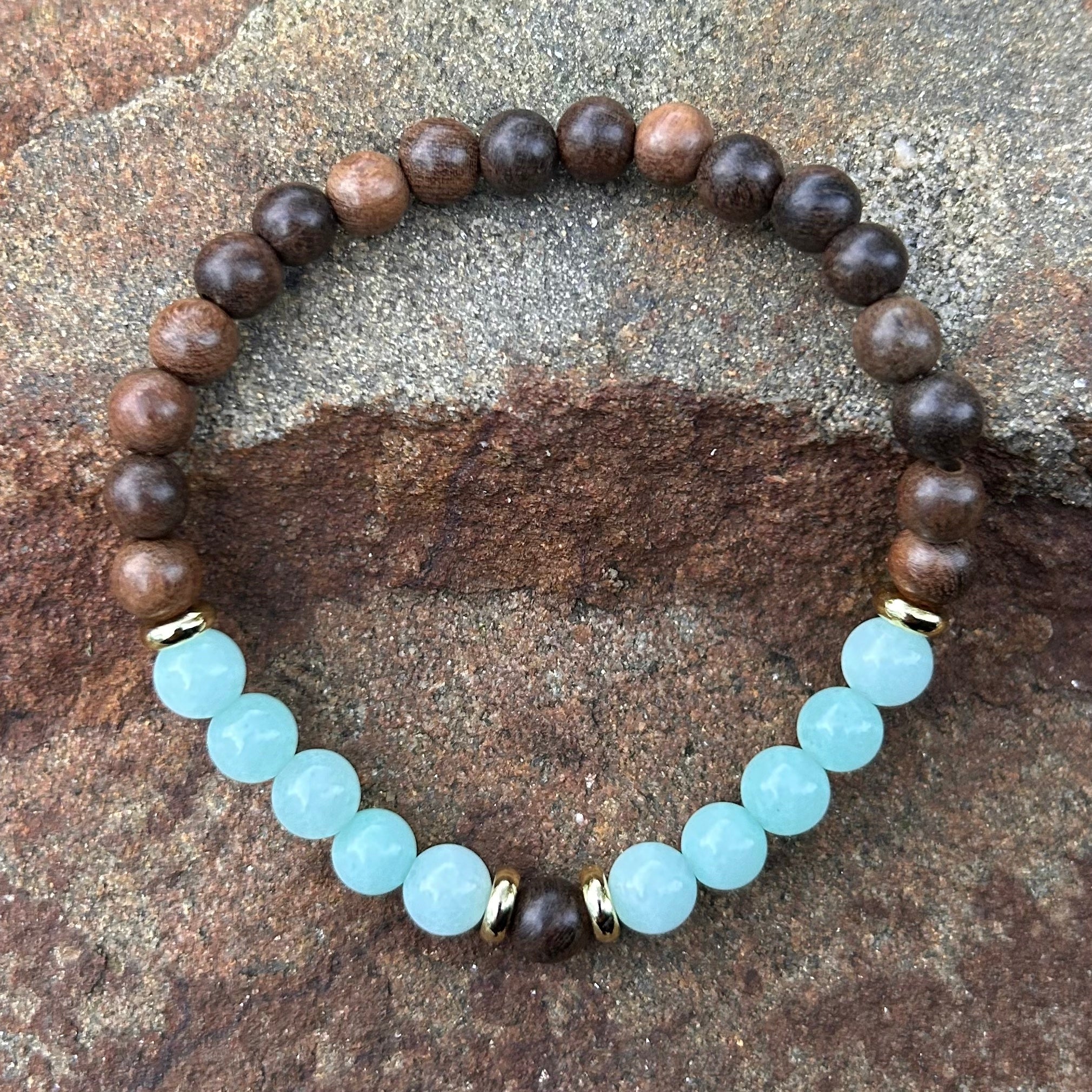 Handgemachtes Armband aus Amazonit und Sandelholz mit vergoldeten Zwischenelementen auf Naturstein-Hintergrund