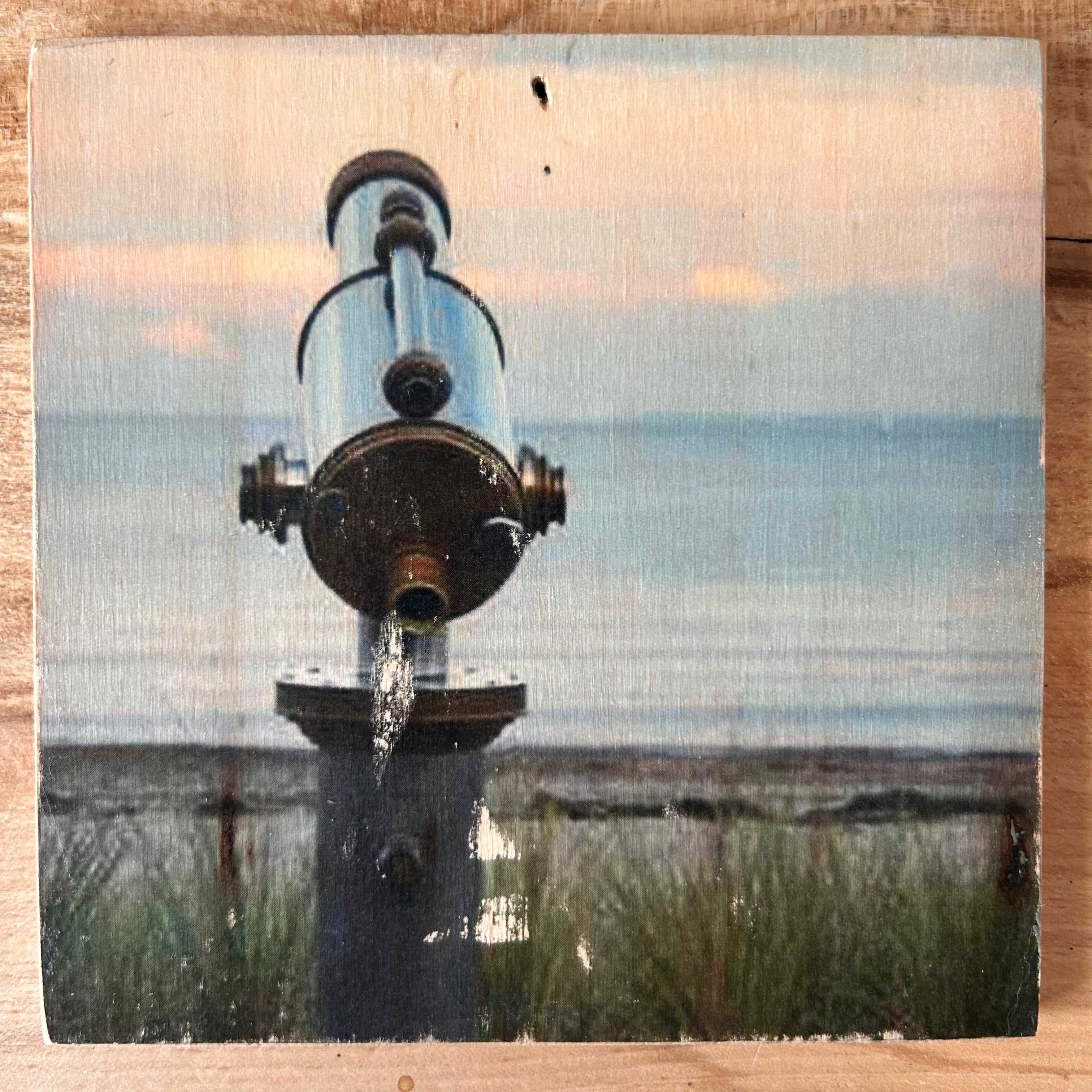 Küstenblick durch ein Fernrohr - dieses Bild bringt dich in Strand- und Meerstimmnung. Im Hintergrund: Dünengras und das Meer. Format 15x15cm. Handgefertigter Fotodruck auf Holz 