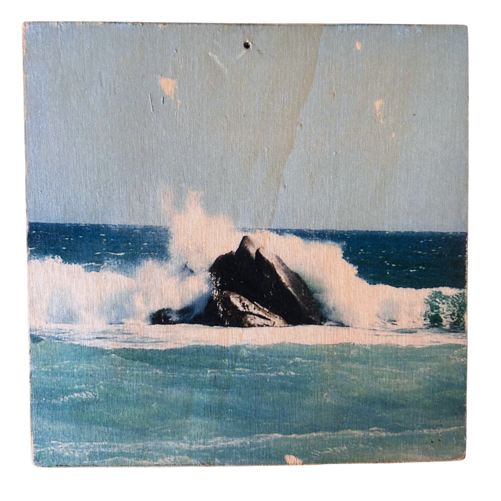 Wellen treffen mitten in einem türkis-blauen Ozean auf einen schraz-braunen Felsen und die Gischt der Wellen spritzen. Format 15x15cm. Handgefertigter Fotodruck auf Holz 