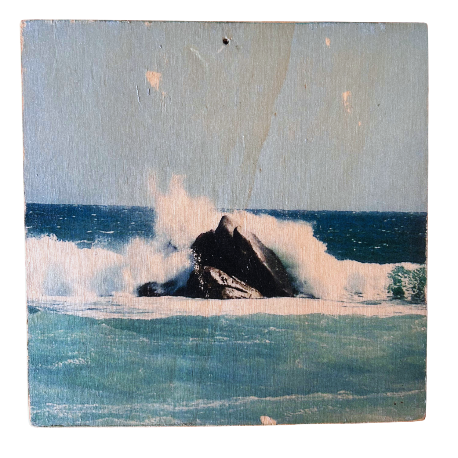 Wellen treffen mitten in einem türkis-blauen Ozean auf einen schraz-braunen Felsen und die Gischt der Wellen spritzen. Format 15x15cm. Handgefertigter Fotodruck auf Holz 