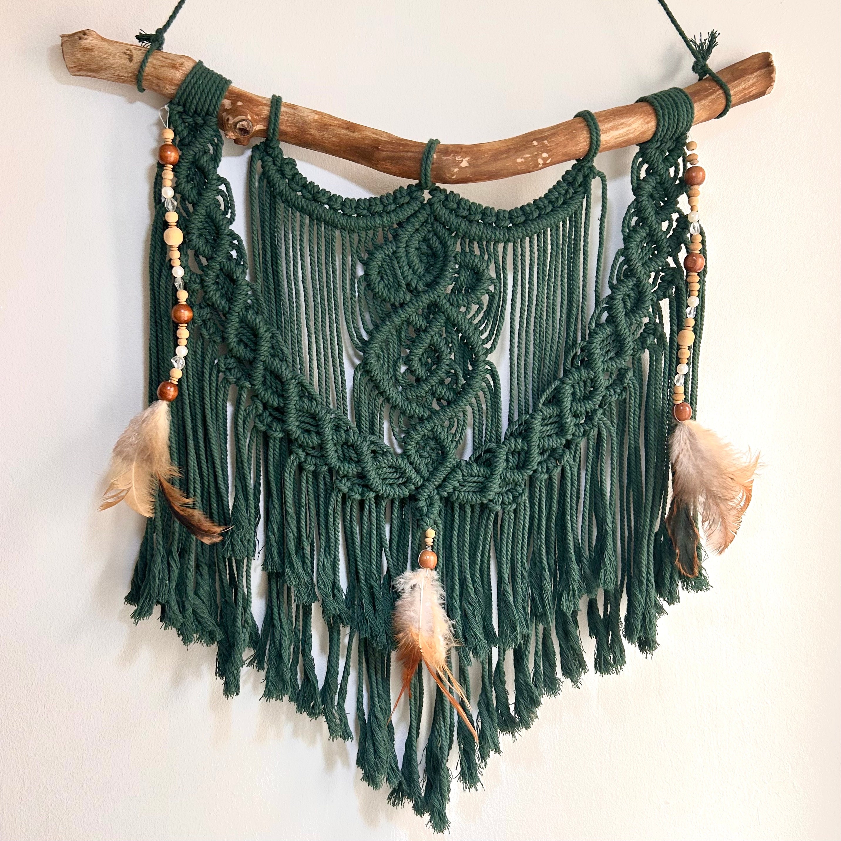 Dunkelgrünes Makramee an Naturholz geknüpft. Verziert mit Perlen und Federn 