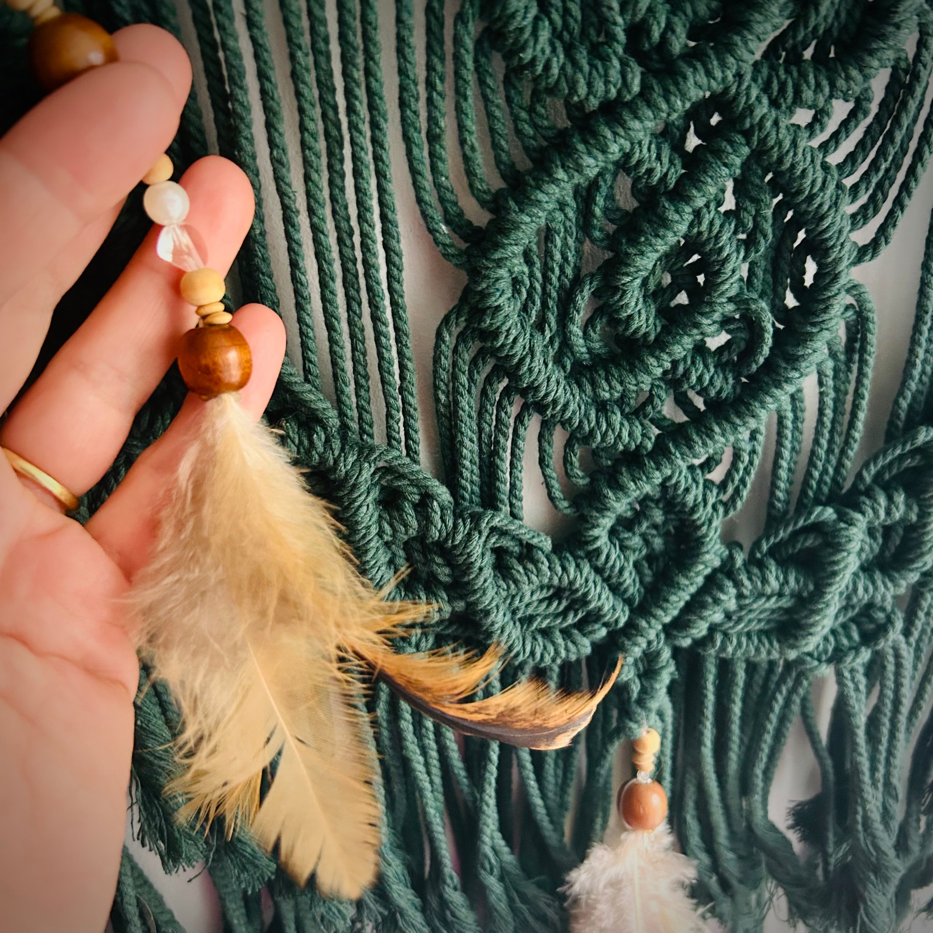 Hand geknüpftes Makramee in dunkelgrün. Verziert mit Perlen und Federn. 