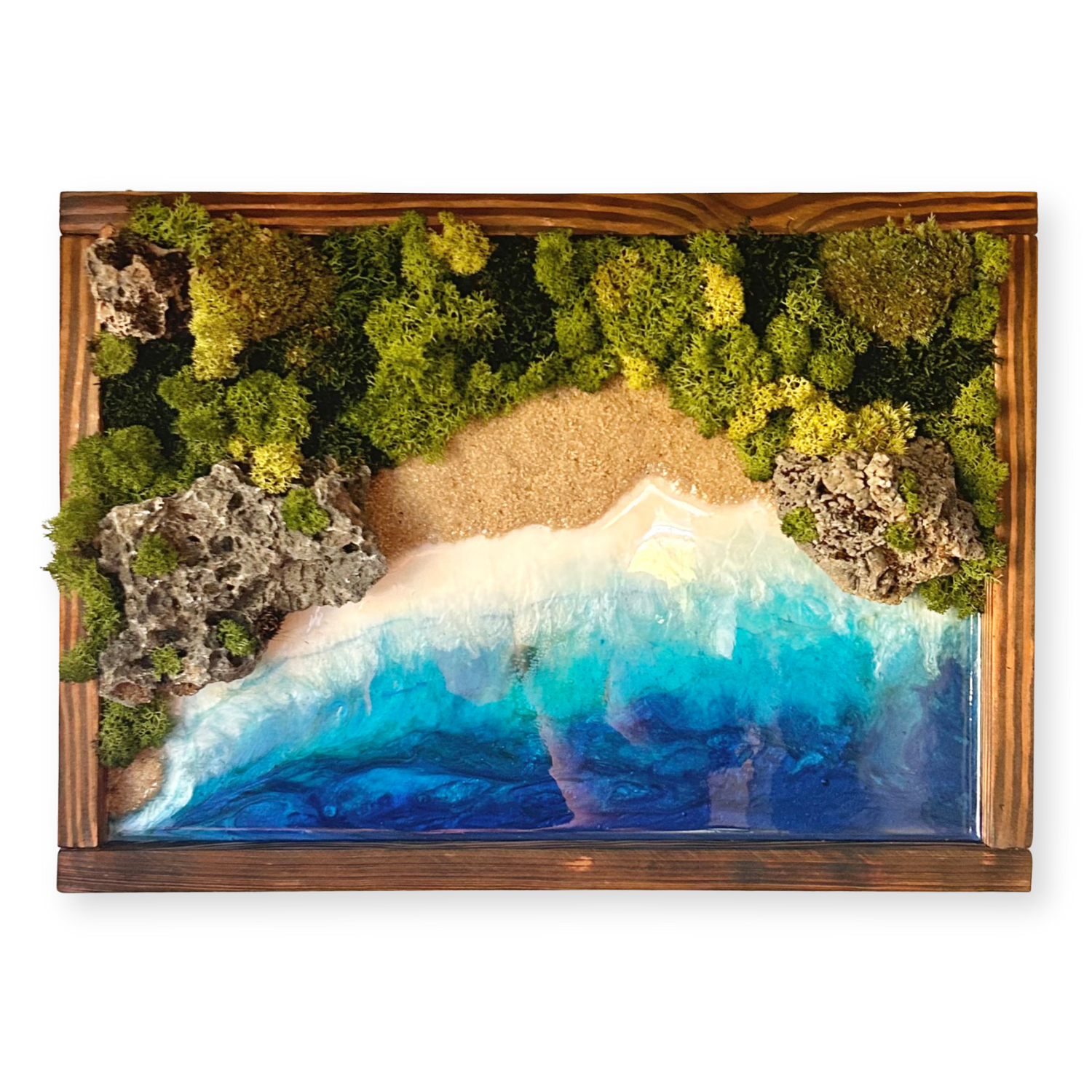 Handgefertigtes Moosbild in einem Rahmen aus geflämmtem Holz, gestaltet wie eine einsame Bucht. Im unteren Bereich schimmert das Meer in Blau- und Türkistöönen aus Epoxidharz, am Ufer ist eine Bucht aus hellem Sand, darüber dichtes, konserviertes Naturmoos als natürlich grüne Landschaft mit dekorativen Lavasteinen. 