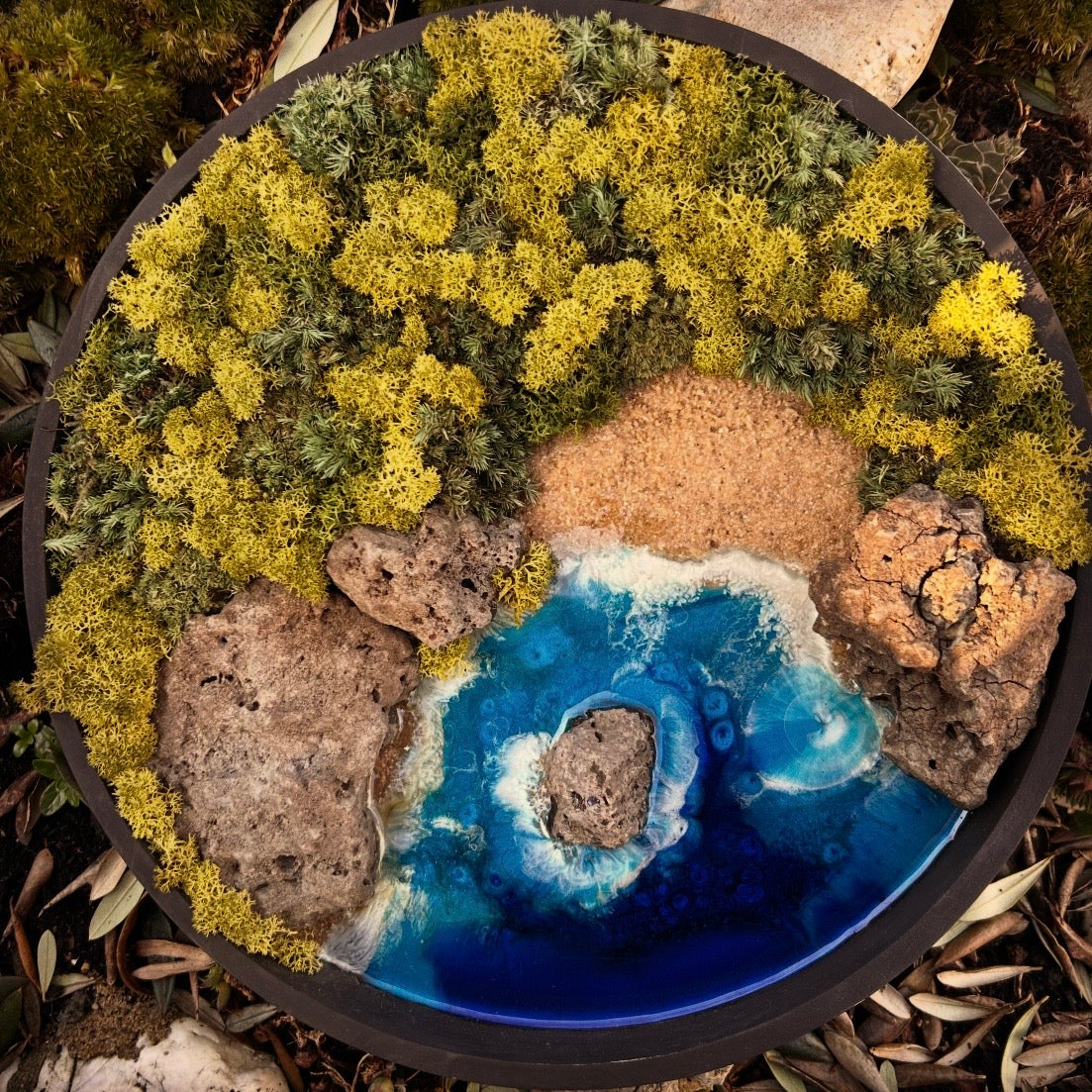 Moosbild mit einer wilden Bucht mit Felsen. Ein Meer aus Resin schlägt Wellen an den Steinen und am Strand. Im Hintergrund befindet sich ein Urwald ausverschiedenen Moosarten. 