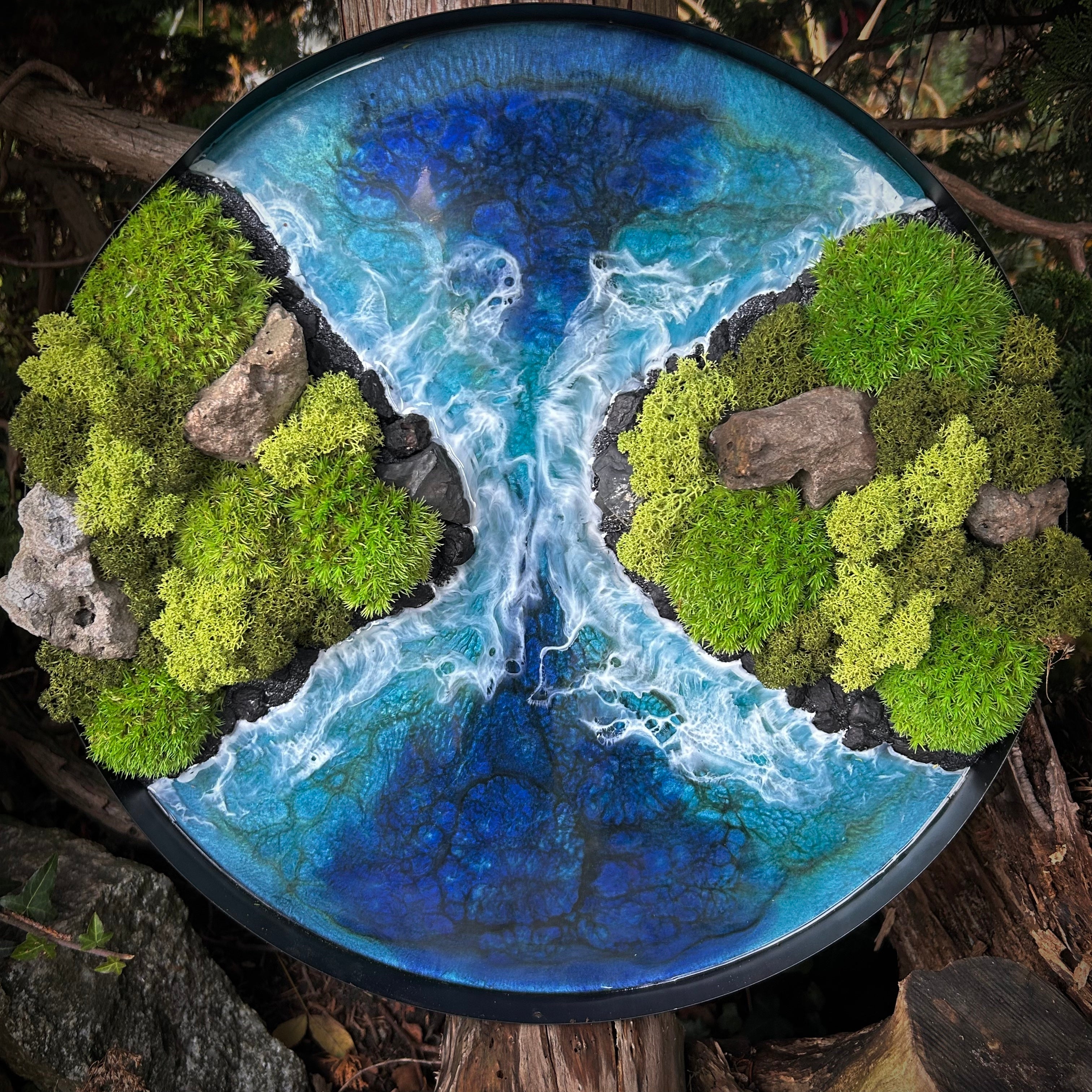 Moosbild mit einem reißenden Meer aus Resin. Das Meer aus Epoxydharz fließt durch eine Meeresenge, gestaltet aus Sand, schwarzen Steinen und Lava. Rechts und Links sind zwei Inseln, bewachsen mit Moos (Kugelmoss und Rentiermoos). Künstlerin: Eva Brandenburg von moos und Meer 