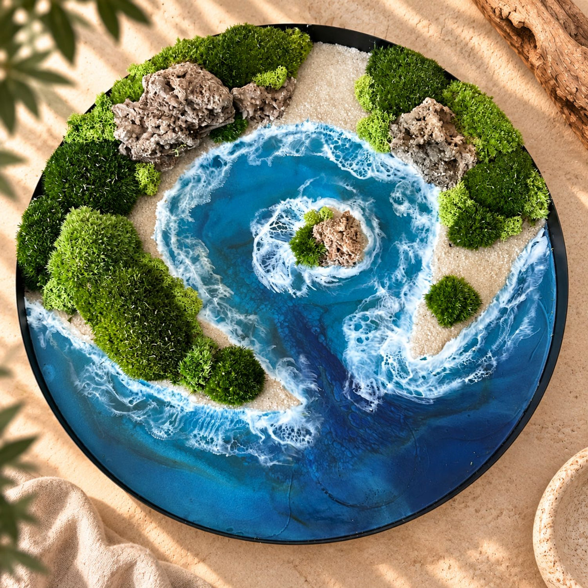 Handgemachtes Moosbild "Blaue Lagune" von Eva Brandenburg, Moos und Meer. Das Bild besteht aus Naturmaterialien: Sand, konserviertem Moos, Natursteinen und einem handgegossenen Meer aus Resin. Es hat einen einem Durchmesser von 40cm. Der Rahmen ist aus Metall. 