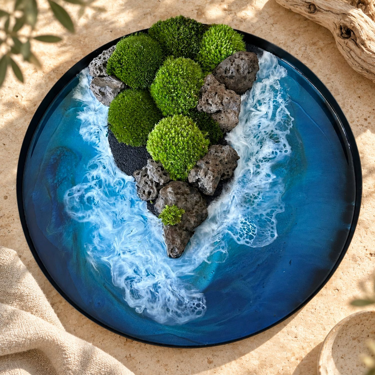Handgemachtes Moosbild "Felsen und Flut" von Eva Brandenburg, Moos und Meer. Das Bild besteht aus Naturmaterialien: Sand, konserviertem Moos, Natursteinen und einem handgegossenen Meer aus Resin. Es hat einen einem Durchmesser von 40cm. Der Rahmen ist aus Metall. 