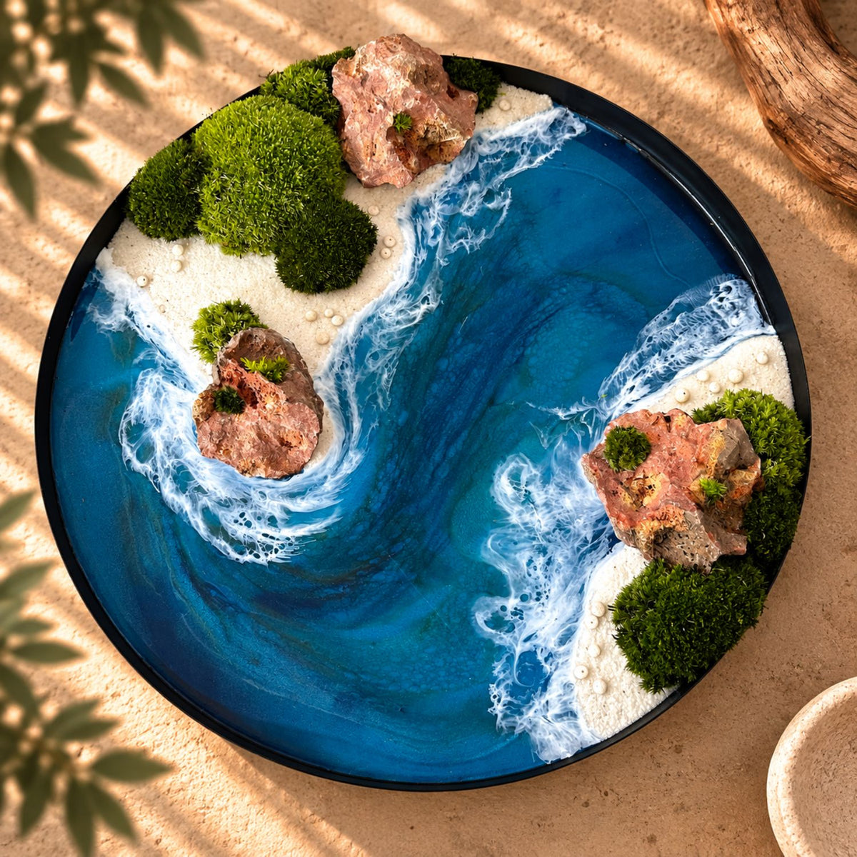 Handgemachtes Moosbild "Flussmündung" von Eva Brandenburg, Moos und Meer. Das Bild besteht aus Naturmaterialien: Sand, konserviertem Moos, Natursteinen und einem handgegossenen Meer aus Resin. Es hat einen einem Durchmesser von 40cm. Der Rahmen ist aus Metall. 