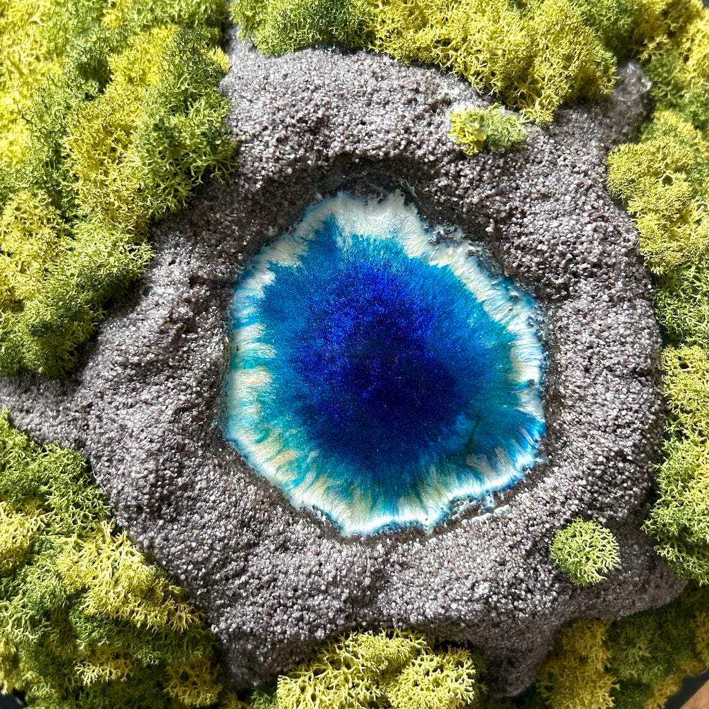 Detailaufnahme des Moosbildes "VulkanSee". Ein Moosbild mit einem von Hand modellierten Vulkan in der Mitte, der sich dimensional aus dem Bilderrahmen heraus bewegt. In der Mitte des Vulkans befindet sich ein Vulkansee aus Resin. 