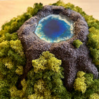 Detailaufnahme 2 des Moosbildes "VulkanSee". Ein Moosbild mit einem von Hand modellierten Vulkan in der Mitte, der sich dimensional aus dem Bilderrahmen heraus bewegt. In der Mitte des Vulkans befindet sich ein Vulkansee aus Resin.