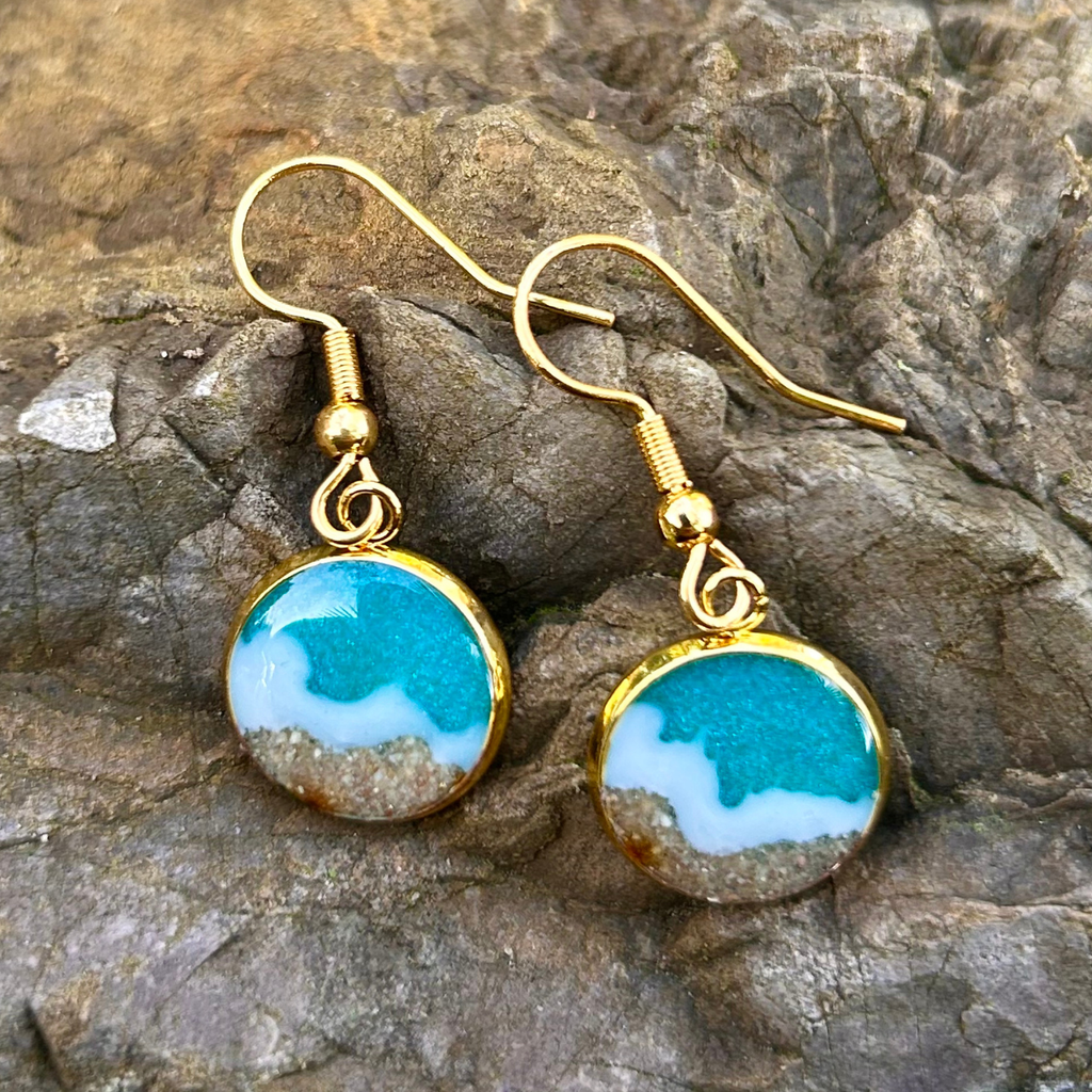 Maritime Hänge-Ohrringe in Gold. Mit Resin wurde ein Meer (türkis mit weißen Wellen) hinein gegossen. Der Strand besteht aus echtem Sand aus Tarifa. 