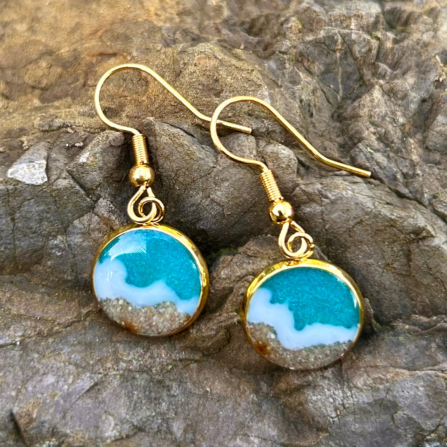 Maritime Hänge-Ohrringe in Gold. Mit Resin wurde ein Meer (türkis mit weißen Wellen) hinein gegossen. Der Strand besteht aus echtem Sand aus Tarifa. 