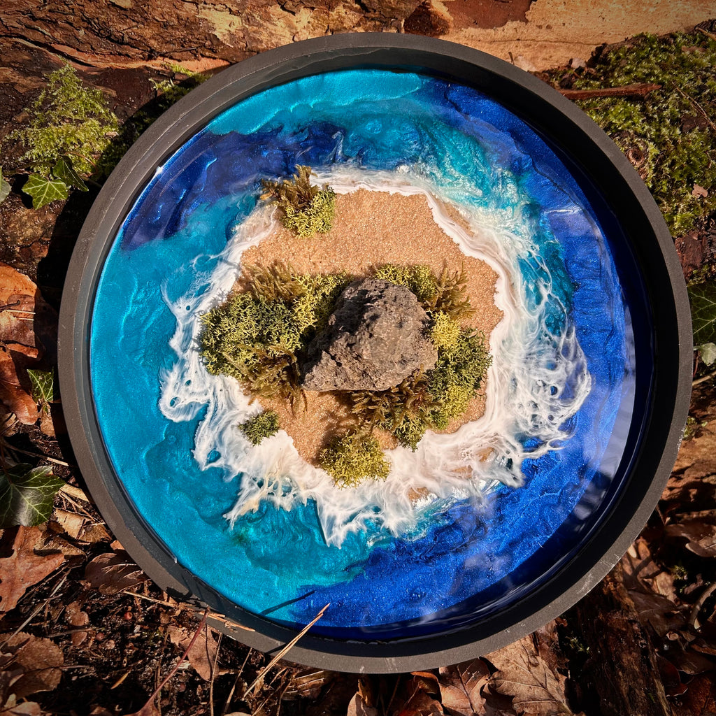 Rundes Moos-und-Meer-Kunstwerk mit kleiner Insel aus Sand, Moos und Stein, umgeben von türkis-blauem Resin-Meer und weißen Wellen, handgefertigte Naturkunst von Moos & Meer