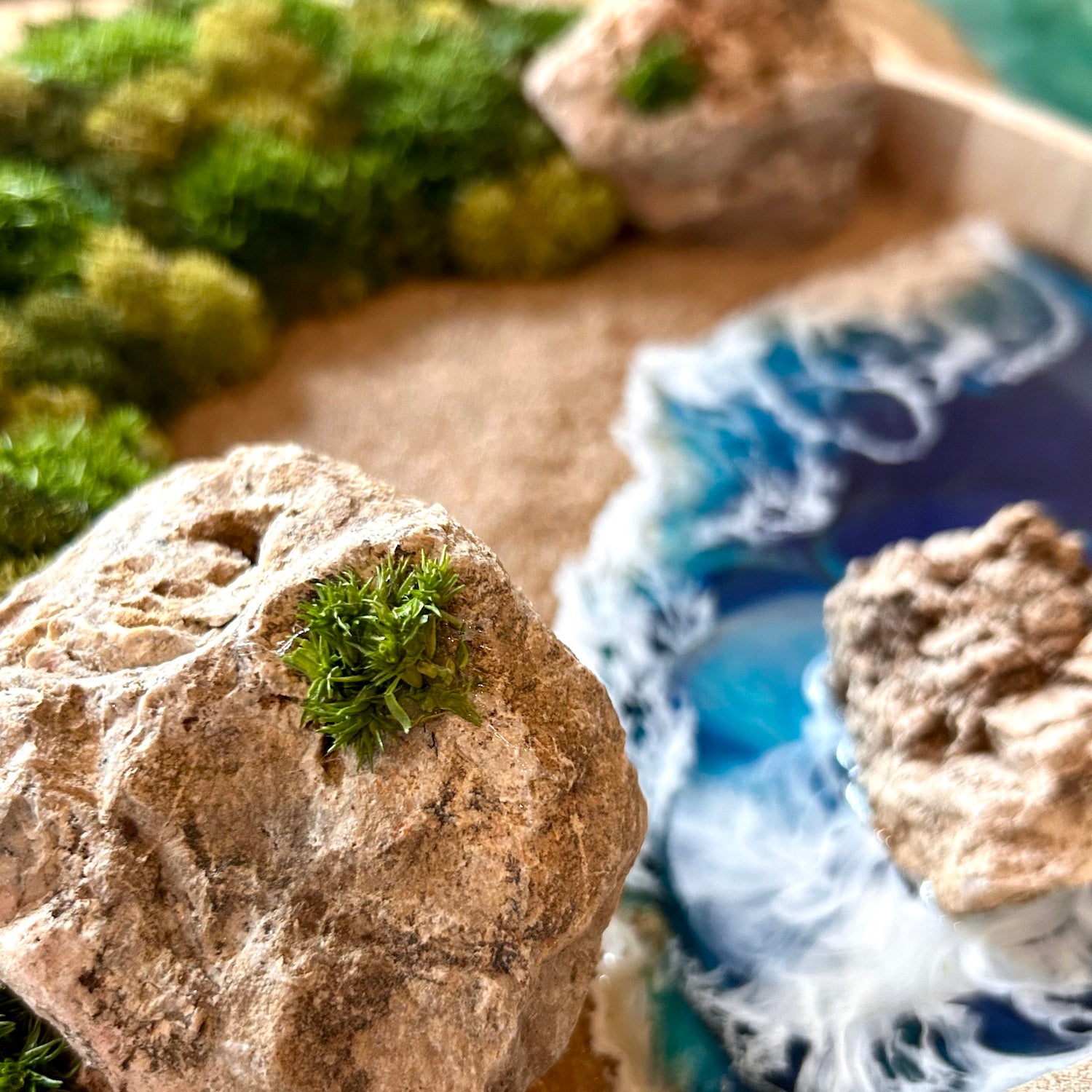 Detailaufnahme 2 des Moosbild "Goldener Strand" . Hier sieht man ein Meer mit Wellen aus Resin, einen Strand mit hellem Sand, Natursteine und grünes, konserviertes Moos. Naturkunst von Moos und Meer in Oberhausen.