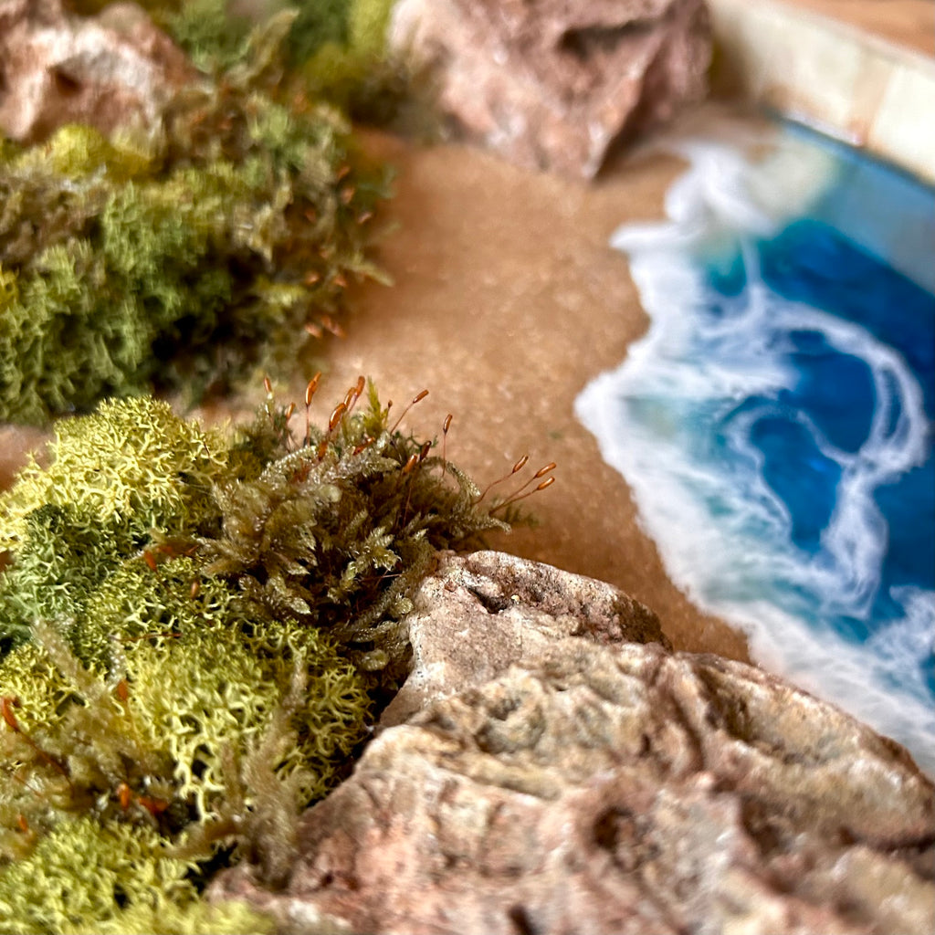Detailaufnahme 2 des Moosbild "Meerpfade" . Hier sieht man ein Meer mit Wellen aus Resin, einen Strand mit hellem Sand, kleine Pfade zwischen den Moosbereichen, Natursteine und grünes, konserviertes Moos. Naturkunst von Moos und Meer in Oberhausen.