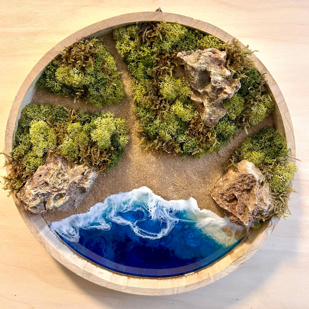 Moosbild "Meerpfade" . Hier sieht man ein Meer mit Wellen aus Resin, einen Strand mit hellem Sand, kleine Pfade zwischen den Moosbereichen, Natursteine und grünes, konserviertes Moos. Naturkunst von Moos und Meer in Oberhausen.