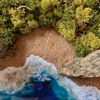 Nahaufnahme vom Moosbild "Strandwächter". Hier sieht man ein Meer mit Wellen aus Resin, einen Strand mit hellem Sand, Natursteine und grünes, konserviertes Moos. Naturkunst von Moos und Meer in Oberhausen.