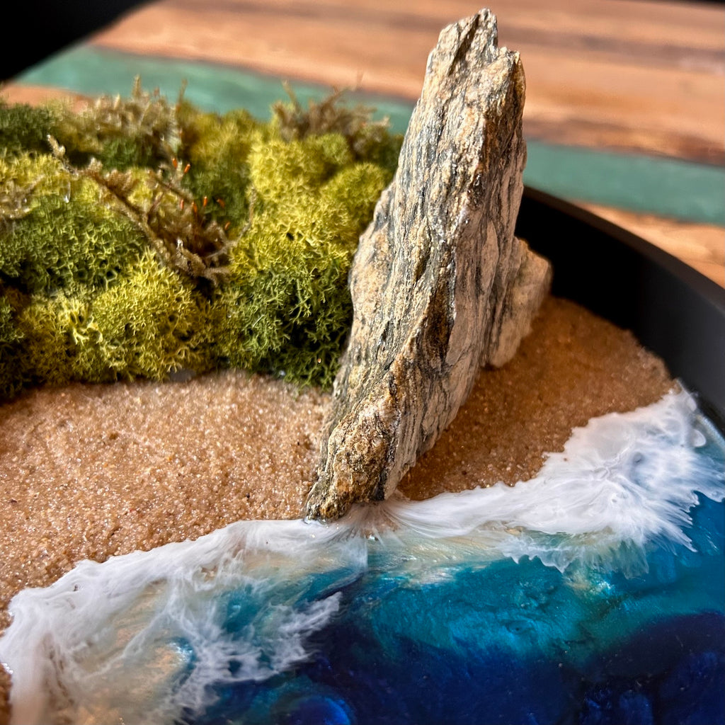 Nahaufnahme 2 vom Moosbild "Strandwächter". Hier sieht man ein Meer mit Wellen aus Resin, einen Strand mit hellem Sand, Natursteine und grünes, konserviertes Moos. Naturkunst von Moos und Meer in Oberhausen.