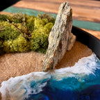 Nahaufnahme 2 vom Moosbild "Strandwächter". Hier sieht man ein Meer mit Wellen aus Resin, einen Strand mit hellem Sand, Natursteine und grünes, konserviertes Moos. Naturkunst von Moos und Meer in Oberhausen.