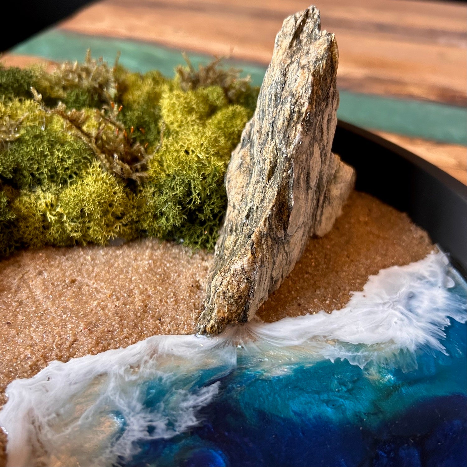 Nahaufnahme 2 vom Moosbild "Strandwächter". Hier sieht man ein Meer mit Wellen aus Resin, einen Strand mit hellem Sand, Natursteine und grünes, konserviertes Moos. Naturkunst von Moos und Meer in Oberhausen.