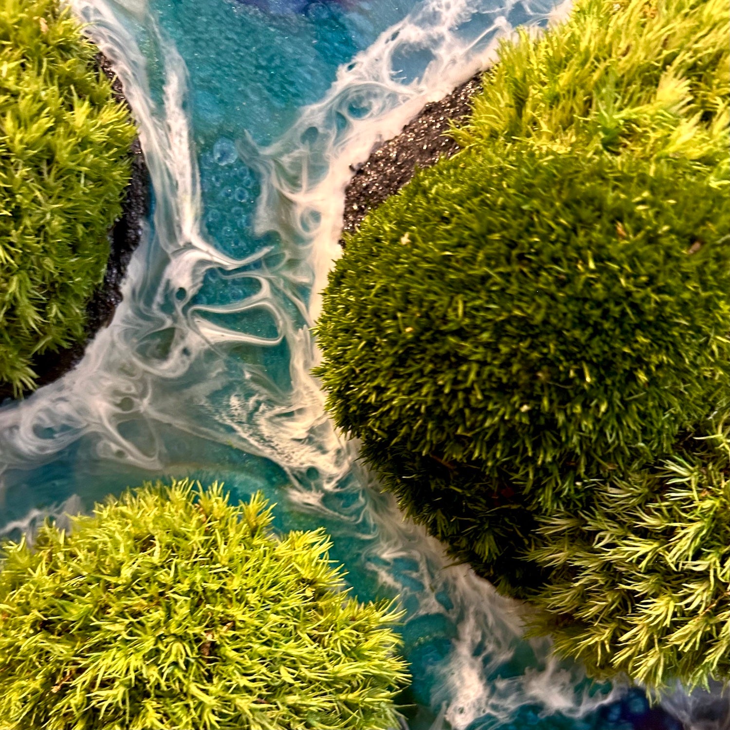 Detailaufnahme des Moosbildes "Waterworld". Hier sieht man ein Meer mit Wellen aus Resin gegossen, Inseln mit schwarzem Sand und grünem, konserviertem Moos. Naturkunst von Moos und Meer in Oberhausen.