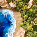 Detailaufnahme 2 des Moosbild "Weitblick" . Hier sieht man ein Meer mit Wellen aus Resin, einen Strand mit hellem Sand, Natursteine und grünes, konserviertes Moos. Naturkunst von Moos und Meer in Oberhausen.