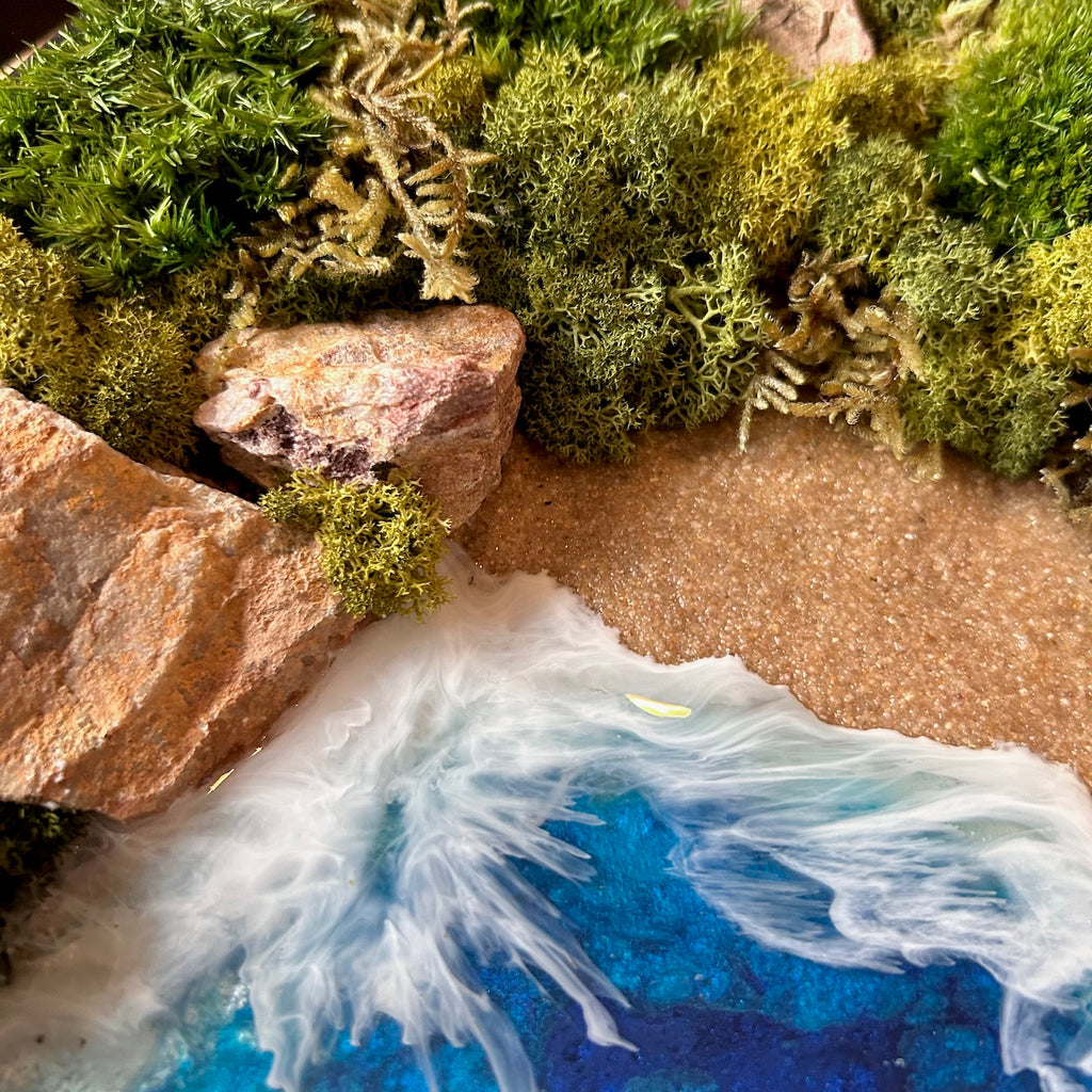 Detailaufnahme des Moosbild "Weitblick" . Hier sieht man ein Meer mit Wellen aus Resin, einen Strand mit hellem Sand, Natursteine und grünes, konserviertes Moos. Naturkunst von Moos und Meer in Oberhausen.