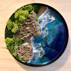 Moosbild "Wellen und Zeit" in einem runden Metallrahmen. Hier sieht man ein Meer mit Wellen aus Resin, einen Strand mit hellem Sand, Natursteine mit einem besonderen Muster und grünes, konserviertes Moos. Naturkunst von Moos und Meer in Oberhausen.