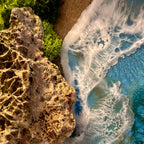 Nahaufnahme vom Moosbild "Wellen und Zeit". Hier sieht man ein Meer mit Wellen aus Resin, einen Strand mit hellem Sand, Natursteine mit einem besonderen Muster und grünes, konserviertes Moos. Naturkunst von Moos und Meer in Oberhausen.