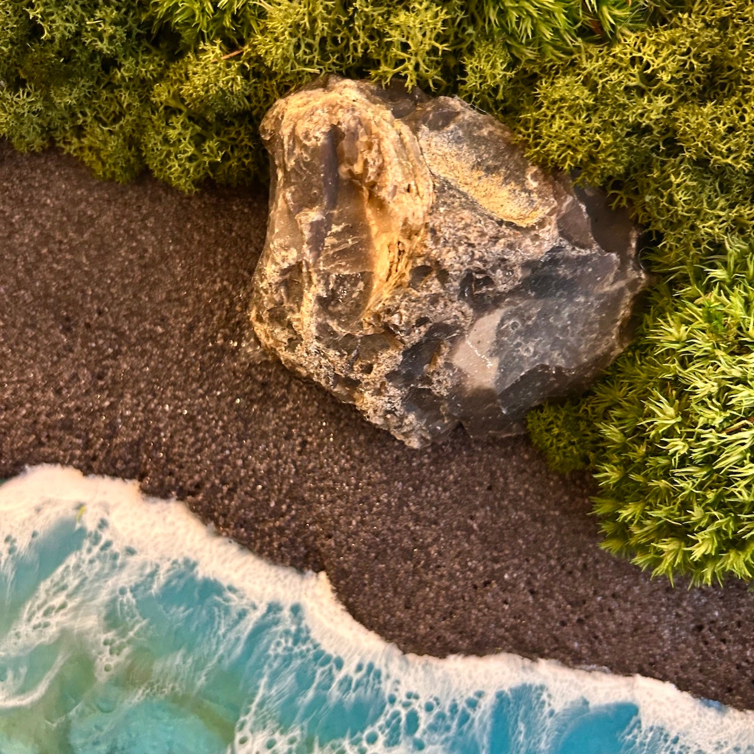Detailaufnahme 2 des Moosbild "Wildes Paradies". Hier sieht man ein Meer mit Wellen aus Resin, einen Strand mit schwarzem Sand, Natursteine und grünes, konserviertes Moos. Naturkunst von Moos und Meer in Oberhausen.