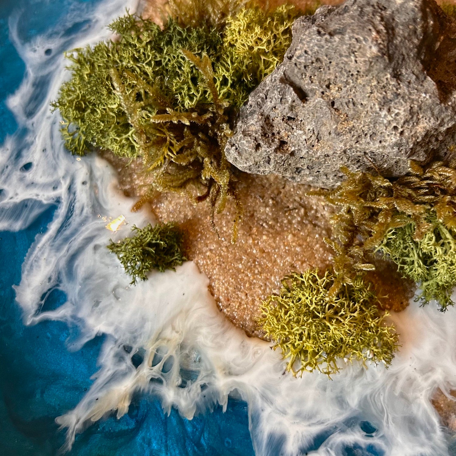 Detailaufnahme 2 des Moosbild "Einsame Insel" . Hier sieht man ein Meer mit Wellen aus Resin, einen Strand mit hellem Sand, Natursteine und grünes, konserviertes Moos. Naturkunst von Moos und Meer in Oberhausen.