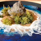 Detailaufnahme des Moosbild "Einsame Insel" . Hier sieht man ein Meer mit Wellen aus Resin, einen Strand mit hellem Sand, Natursteine und grünes, konserviertes Moos. Naturkunst von Moos und Meer in Oberhausen.