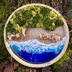 Moosbild "Treibholzstrand" in einem runden Rahmen aus Bahmbus, aufgenommen im Wald. Hier sieht man ein Meer mit Wellen aus Resin, einen Strand mit hellem Sand, Treibholz und grünes, konserviertes Moos. Naturkunst von Moos und Meer in Oberhausen.